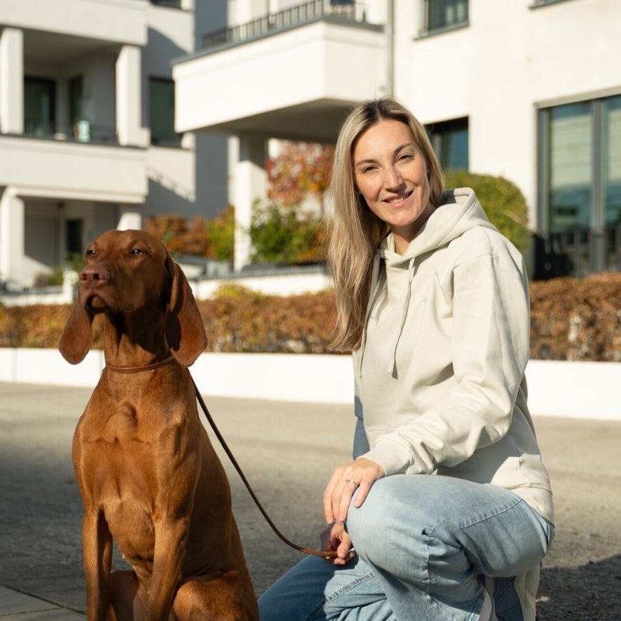 World of Dogs - Das Foto zeigt eine Frau die einen grauen Hoodie trägt von World of dogs. Daneben sitzt ein Magyar Vizsla