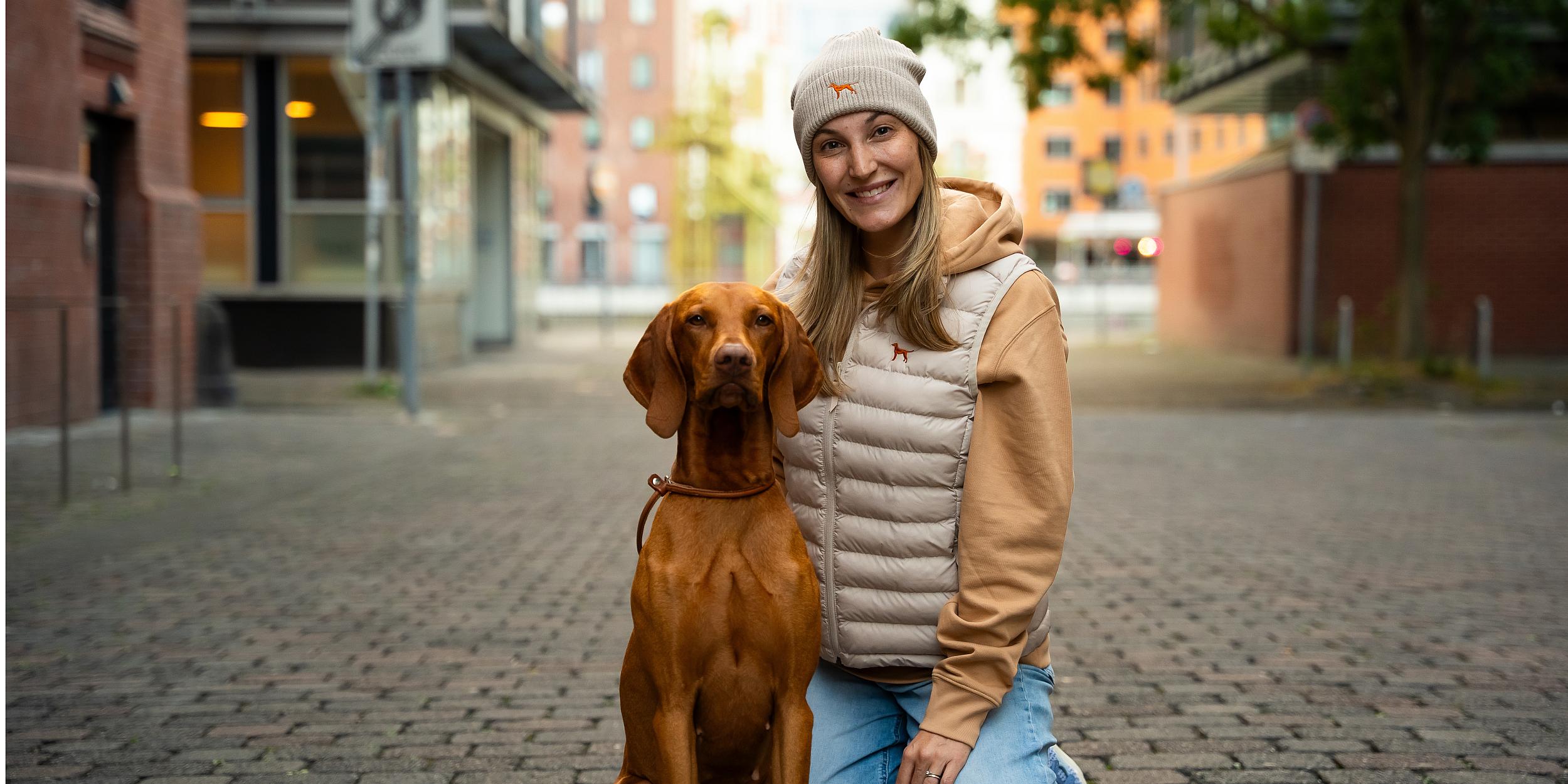 hier wird ein magyar vizsla gezeigt und eine frau, die eine mütze, hoodie und weste trägt von world of dogs mit vizsla stickerei